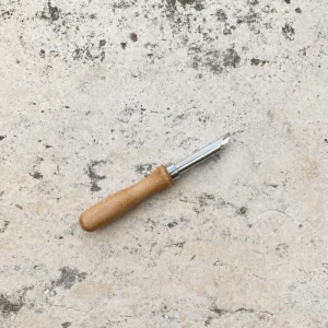 Wooden handled greenware punch tool on a stone surface