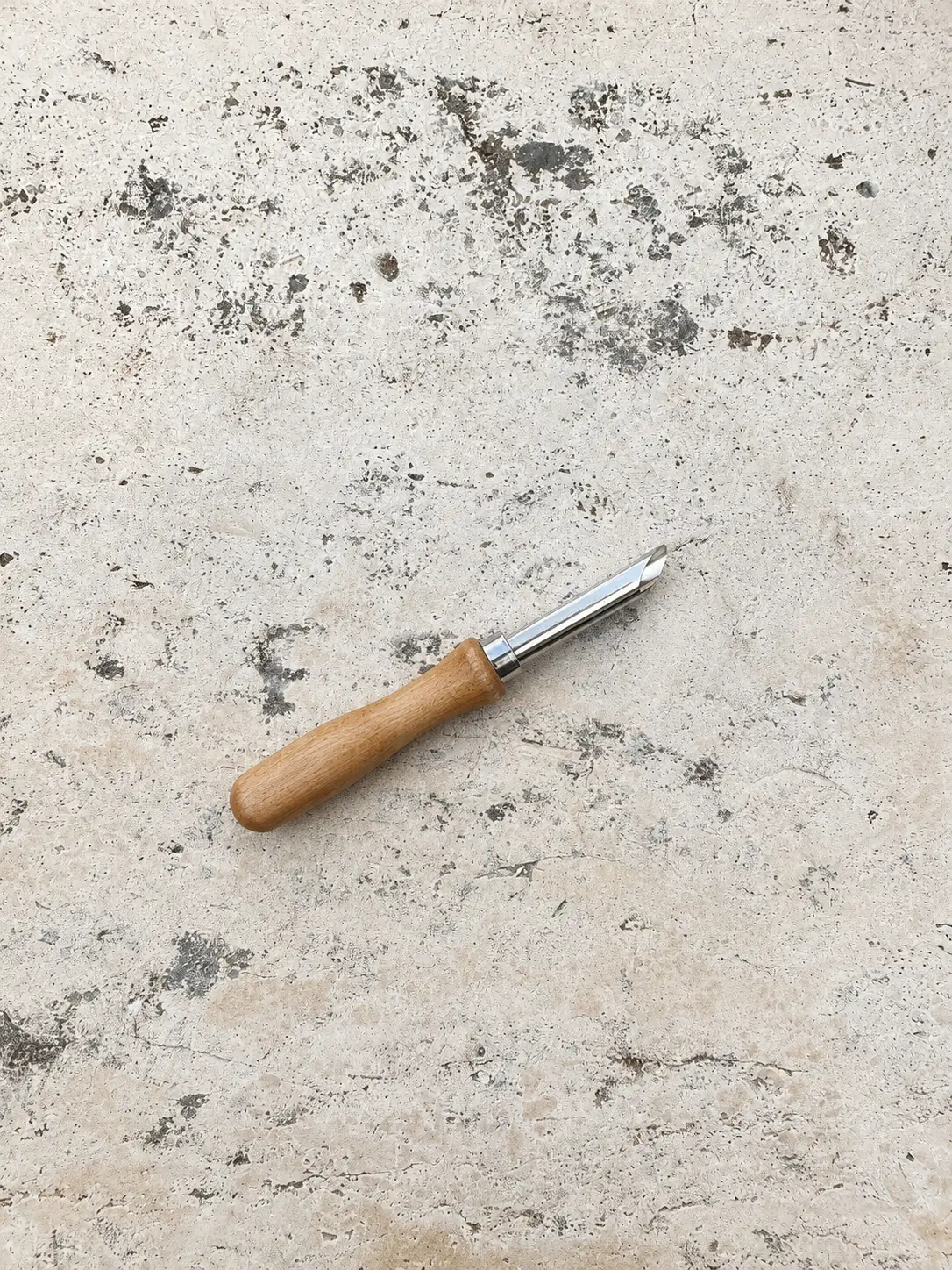 Wooden handled greenware punch tool on a stone surface