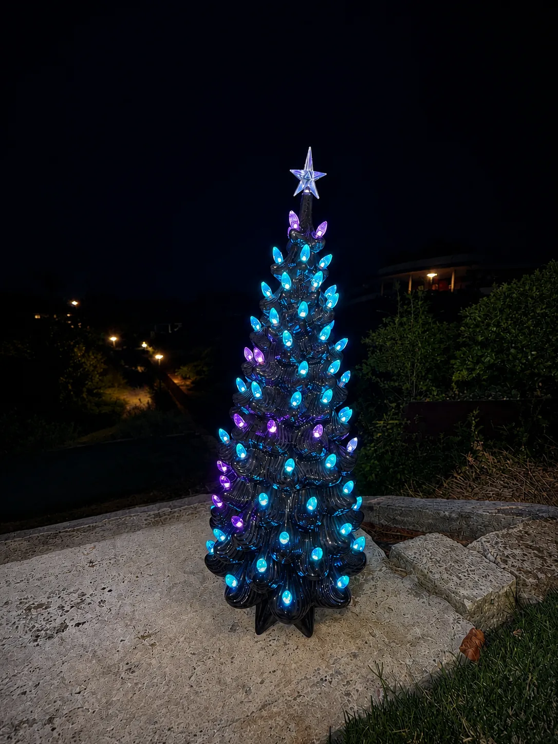 Black ceramic tree lit blue and purple outdoors at night