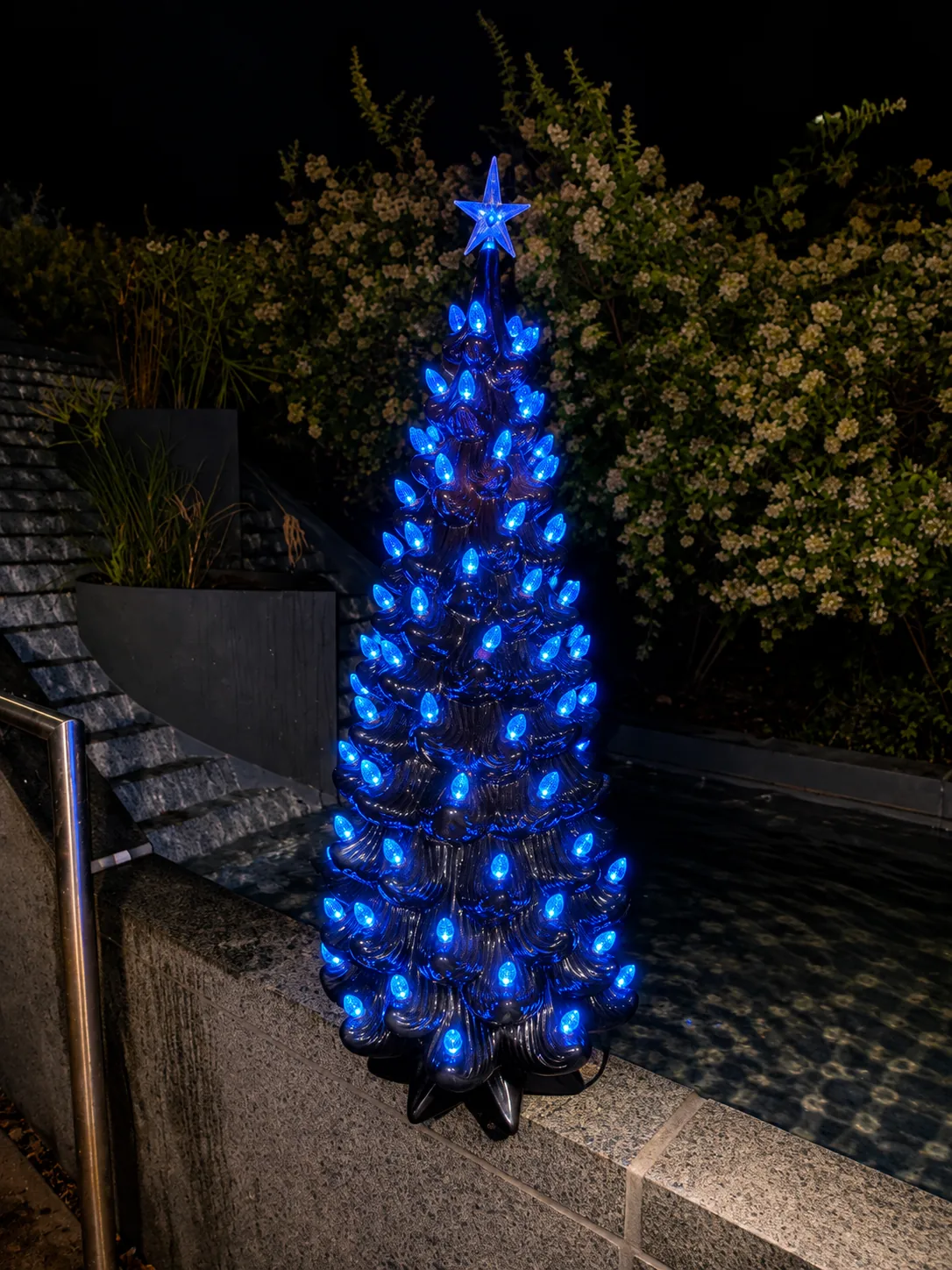 Ceramic tree lit all blue beside a pool at night